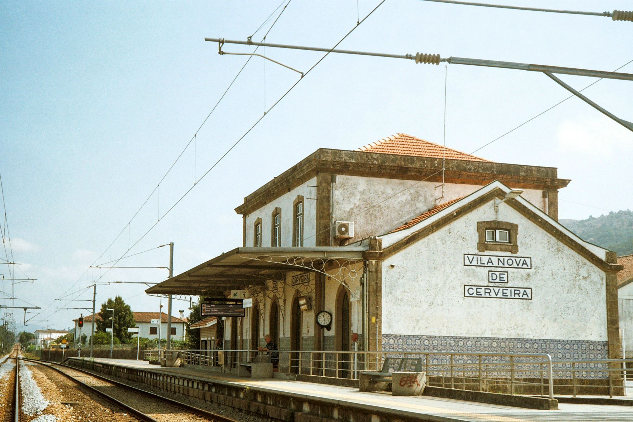 Vila Nova de Cerveira railway station: a whitewashed building with blue azulejo tiles, a platform clock, and overhead wires above the tracks.